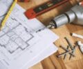 Close-up of construction blueprint with tools like drill and screws on a wooden table.