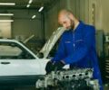 Mechanic in a blue coverall inspecting car engine in a garage workshop.